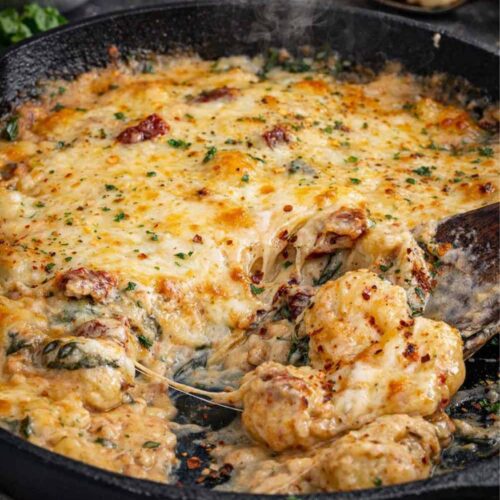 Creamy Tuscan gnocchi bake in a cast iron skillet with melted cheese, sun-dried tomatoes, spinach, and rich garlic sauce.