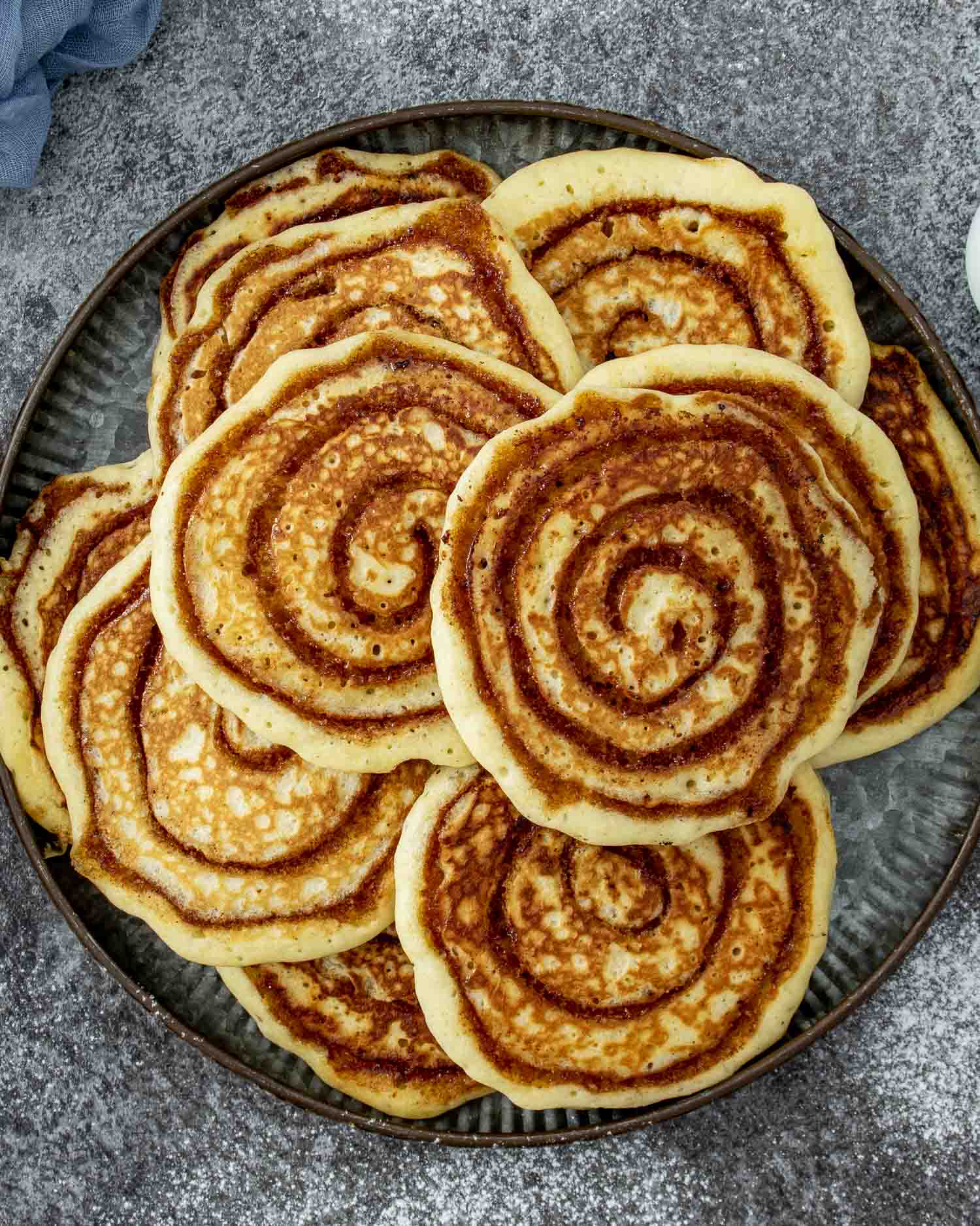 Large platter filled with multiple cinnamon swirl pancakes, overlapping to show distinct golden brown spiraled centers.