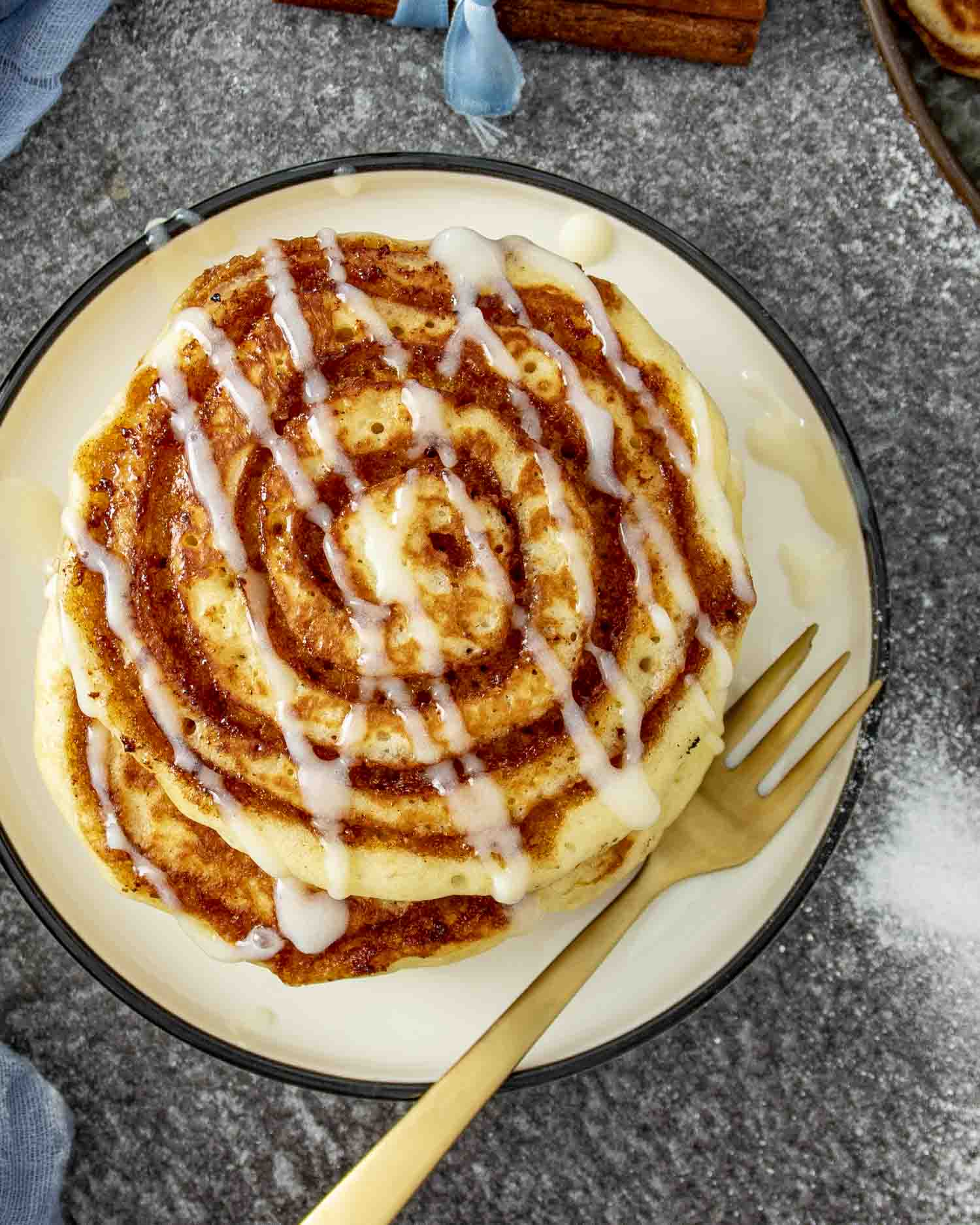 Overhead shot of single pancake on plate with fork, thick glaze drizzle and cinnamon sugar spiral.