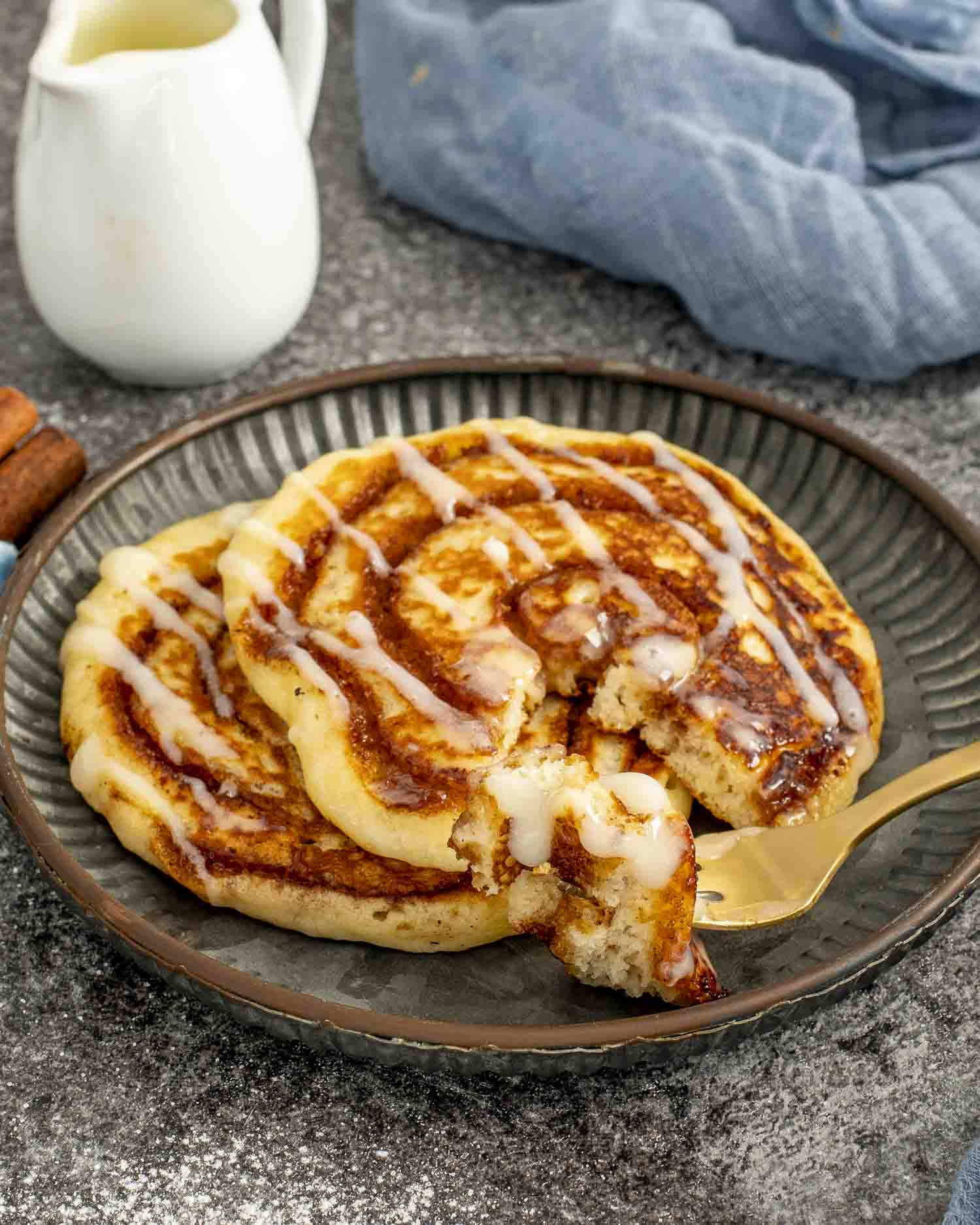 Stack of cinnamon swirl pancakes drizzled with cream cheese glaze, served on a plate with fork.