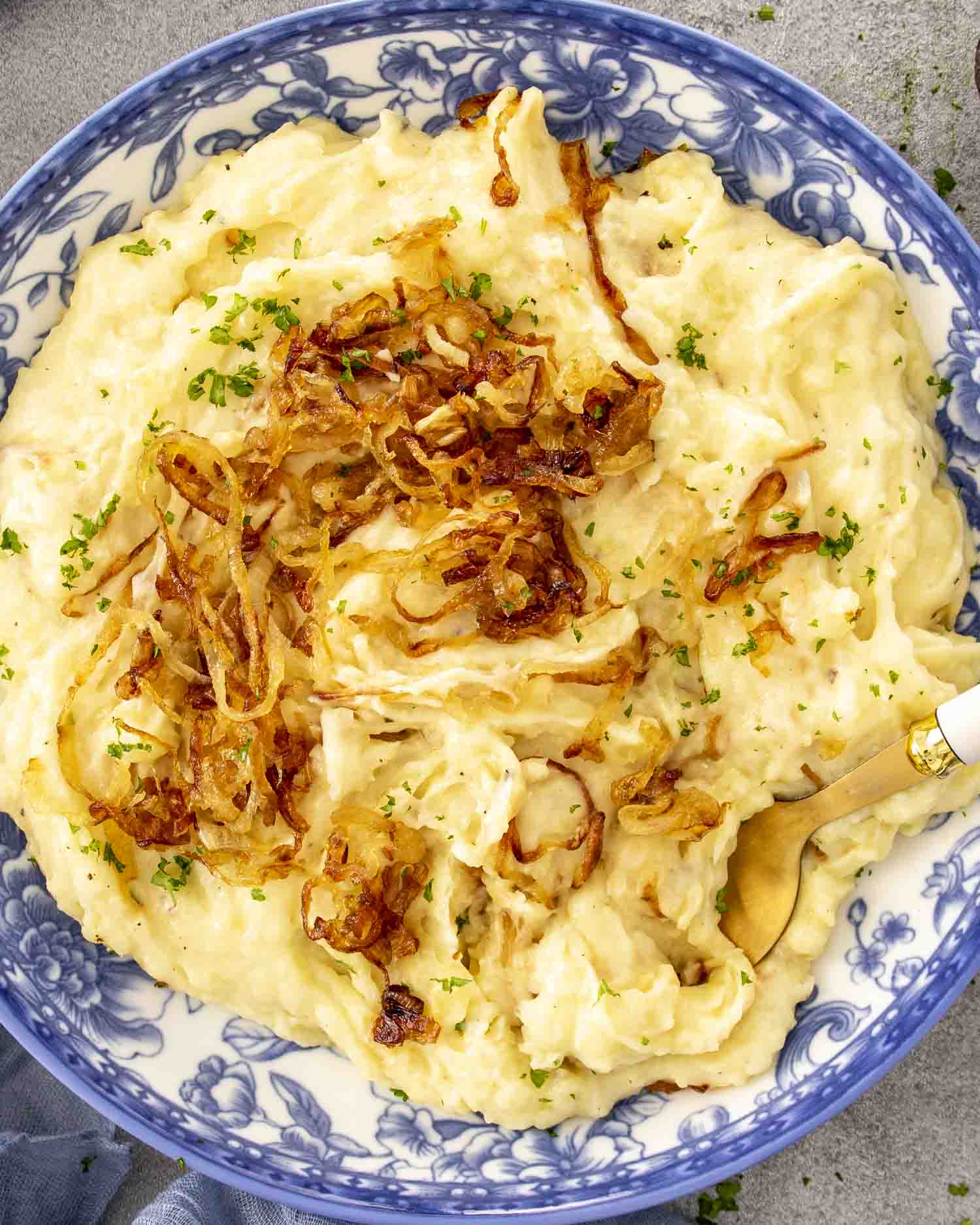 Overhead view of creamy mashed potatoes with Gruyère and caramelized onions in a blue bowl with gold fork.