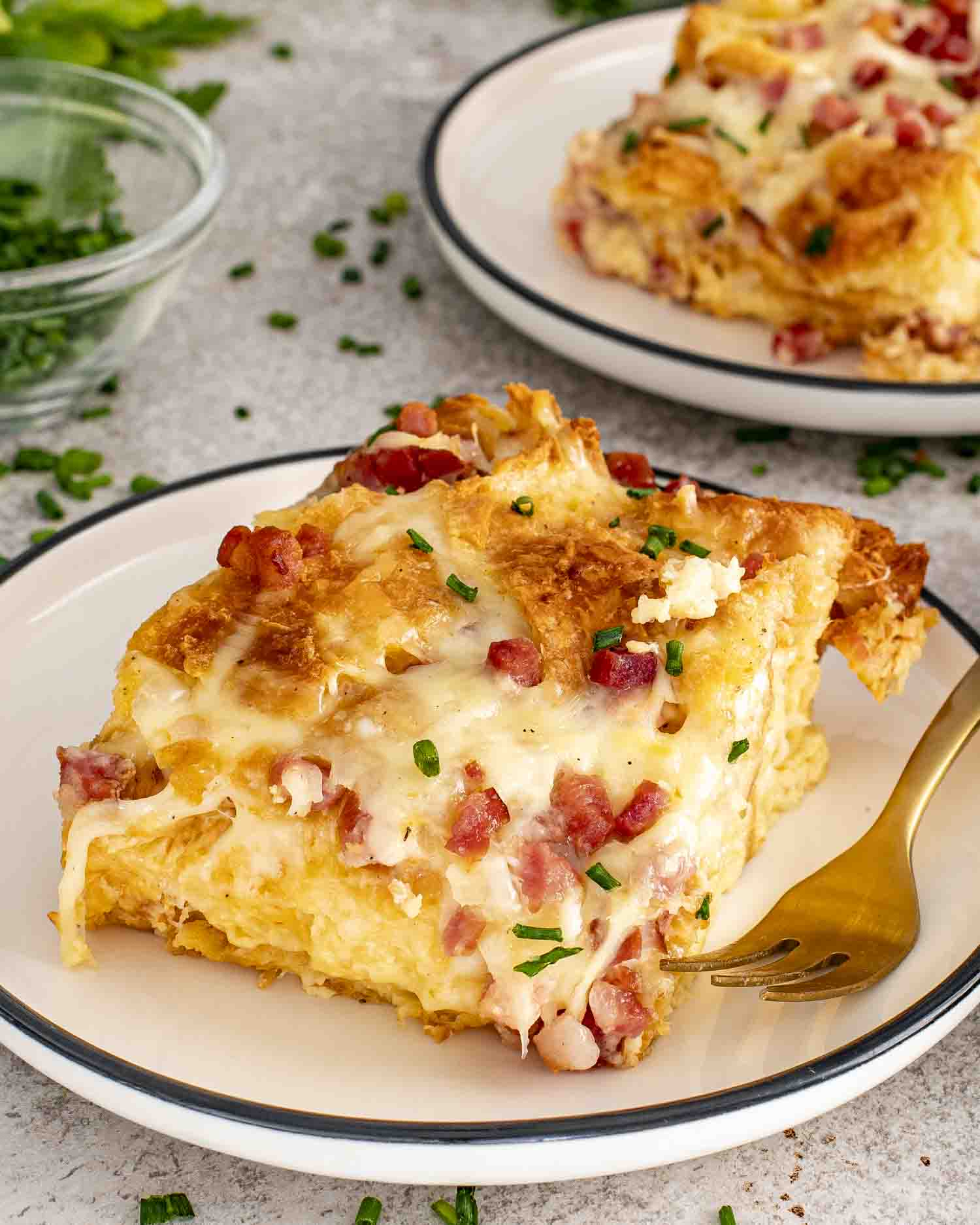 Fork beside square serving of ham and cheese croissant bake with melted cheese and diced ham topping.
