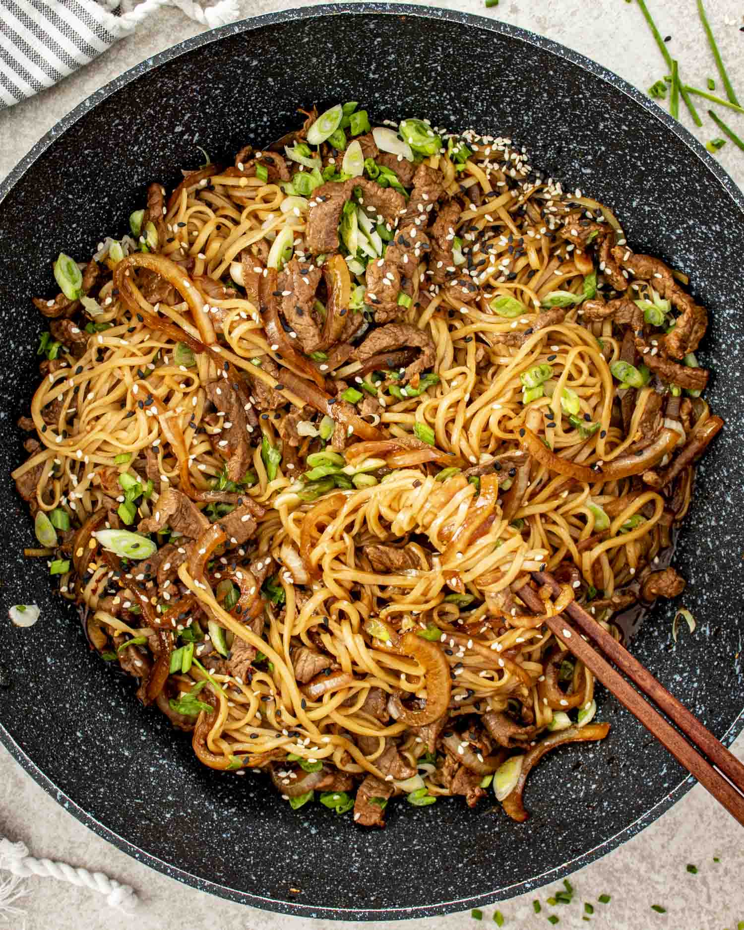 A deep wok brimming with saucy Mongolian beef noodles, sesame seeds, and sliced green onions ready to serve.
