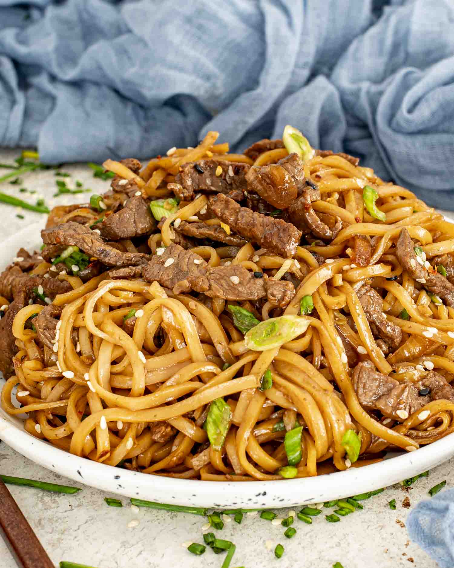A white plate piled high with Mongolian beef noodles, glistening sauce, sesame seeds, and scallions.