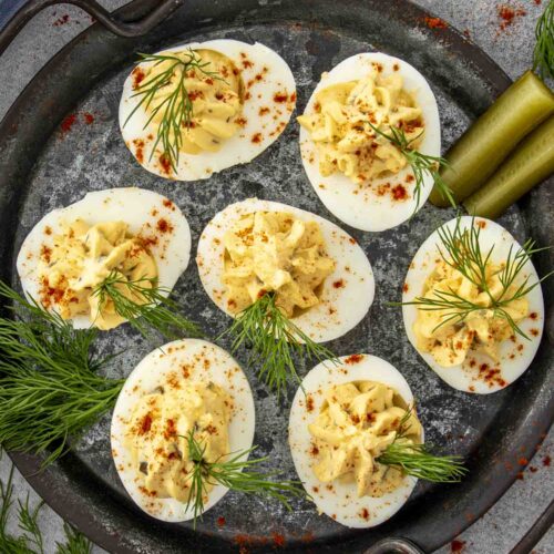 Overhead view of deviled eggs neatly arranged on slate, with pickle spears and scattered dill sprigs.