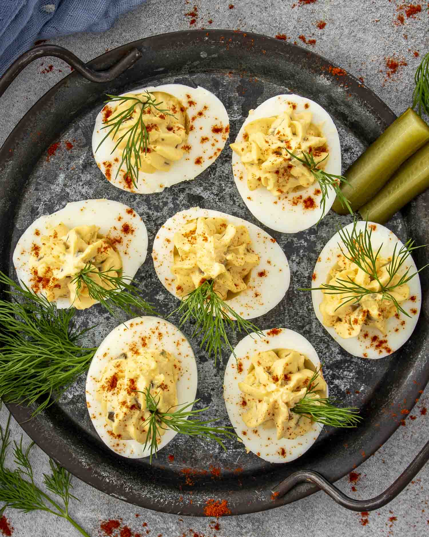 Overhead view of deviled eggs neatly arranged on slate, with pickle spears and scattered dill sprigs.