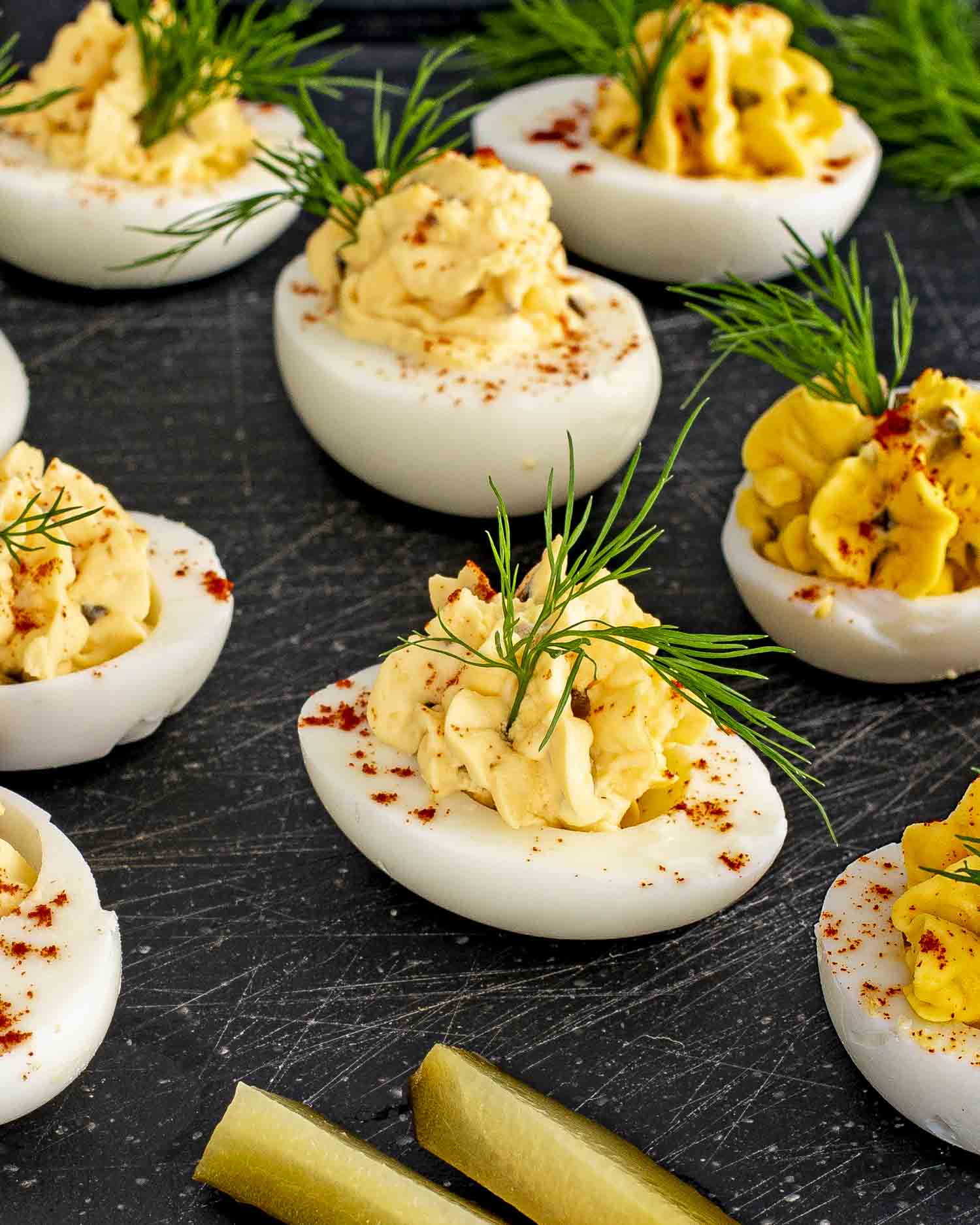 Close-up of deviled eggs on a dark tray, with paprika and fresh dill for a pop of color.