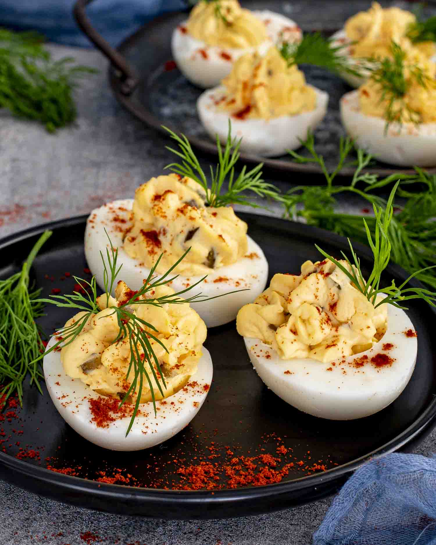 Close-up of deviled eggs on a dark tray, with paprika and fresh dill for a pop of color.