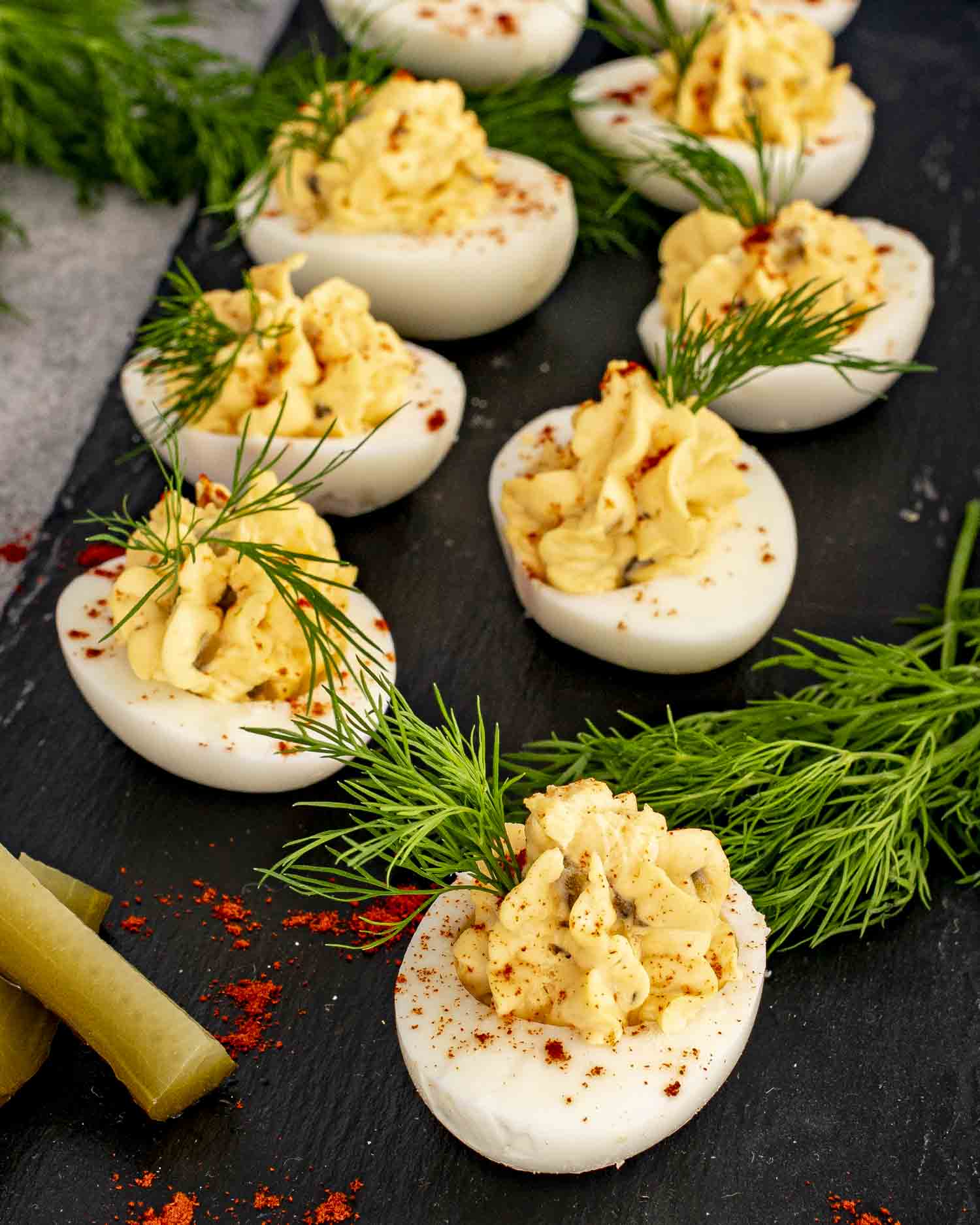 Southern deviled eggs piped with creamy filling, sprinkled with paprika, and garnished with dill on slate board.
