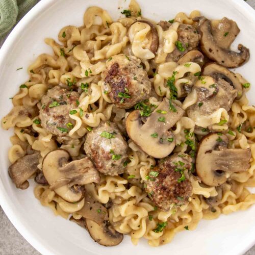 Overhead view of Swedish meatball stroganoff served in white bowl with mushrooms and fresh chopped parsley garnish.