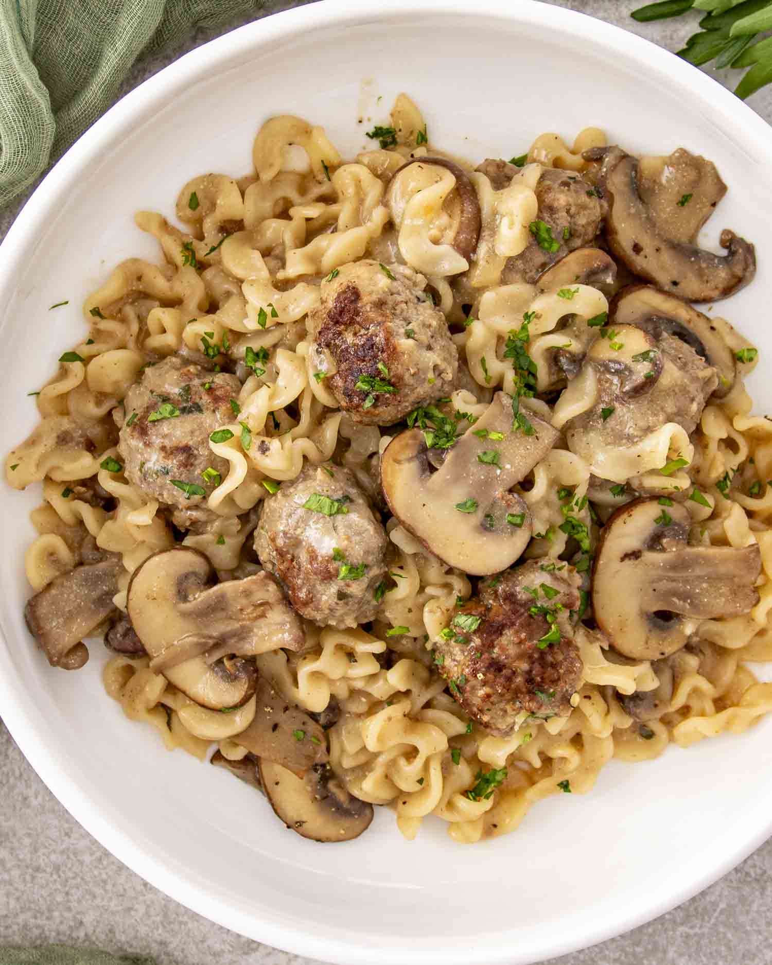 Overhead view of Swedish meatball stroganoff served in white bowl with mushrooms and fresh chopped parsley garnish.