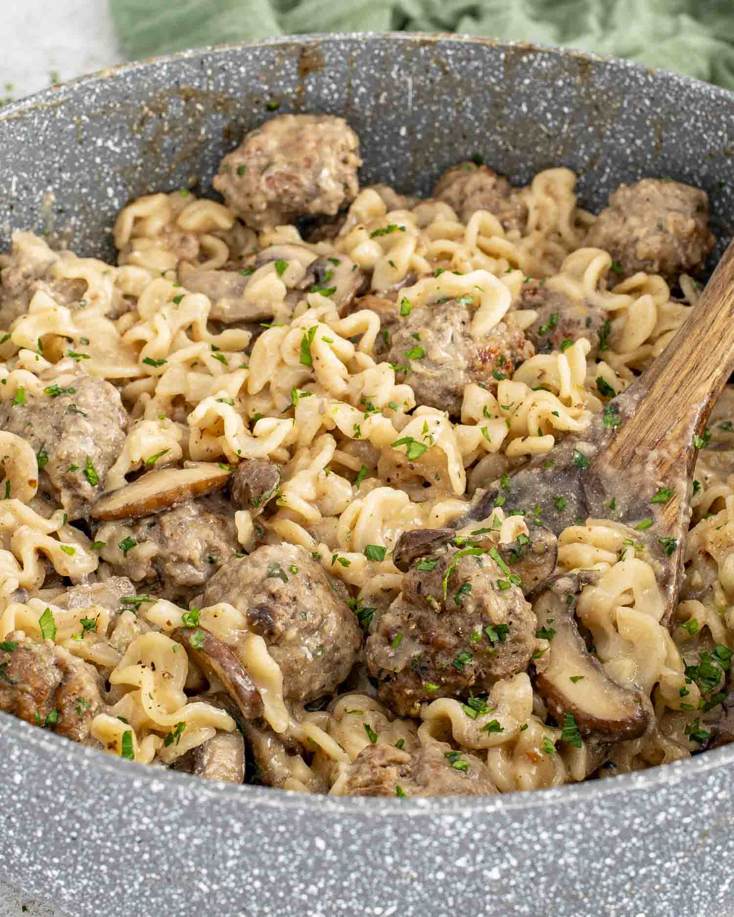 Large skillet of creamy Swedish meatball stroganoff with mushrooms and noodles, wooden spoon resting inside pan.