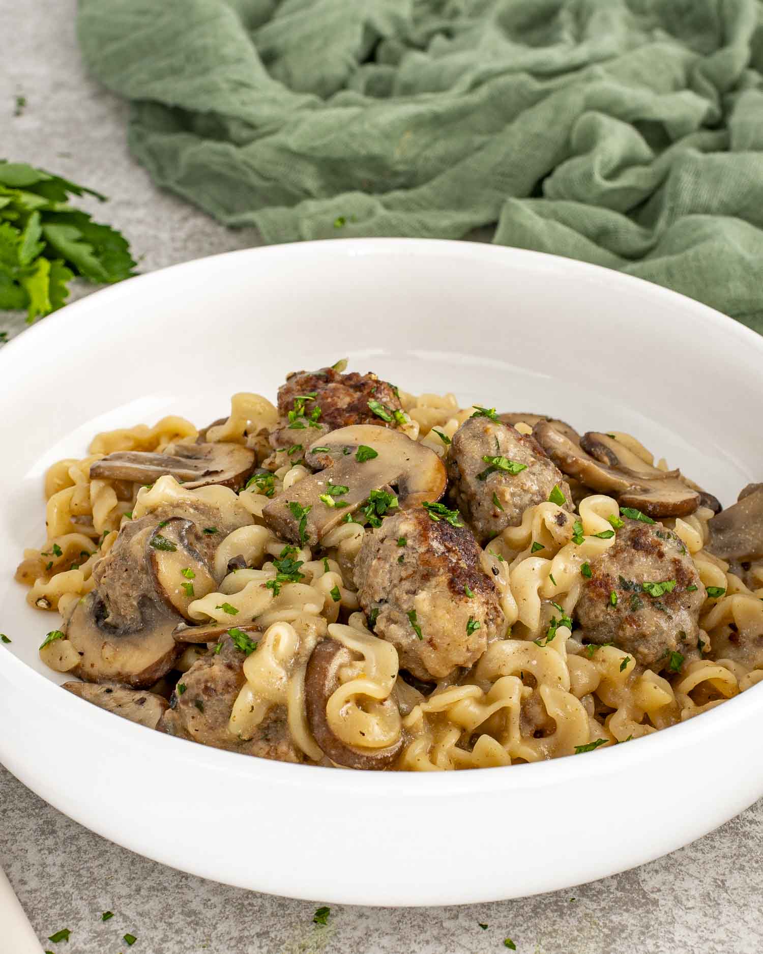 White bowl filled with Swedish meatball stroganoff, egg noodles, mushrooms, and parsley, set on neutral background.