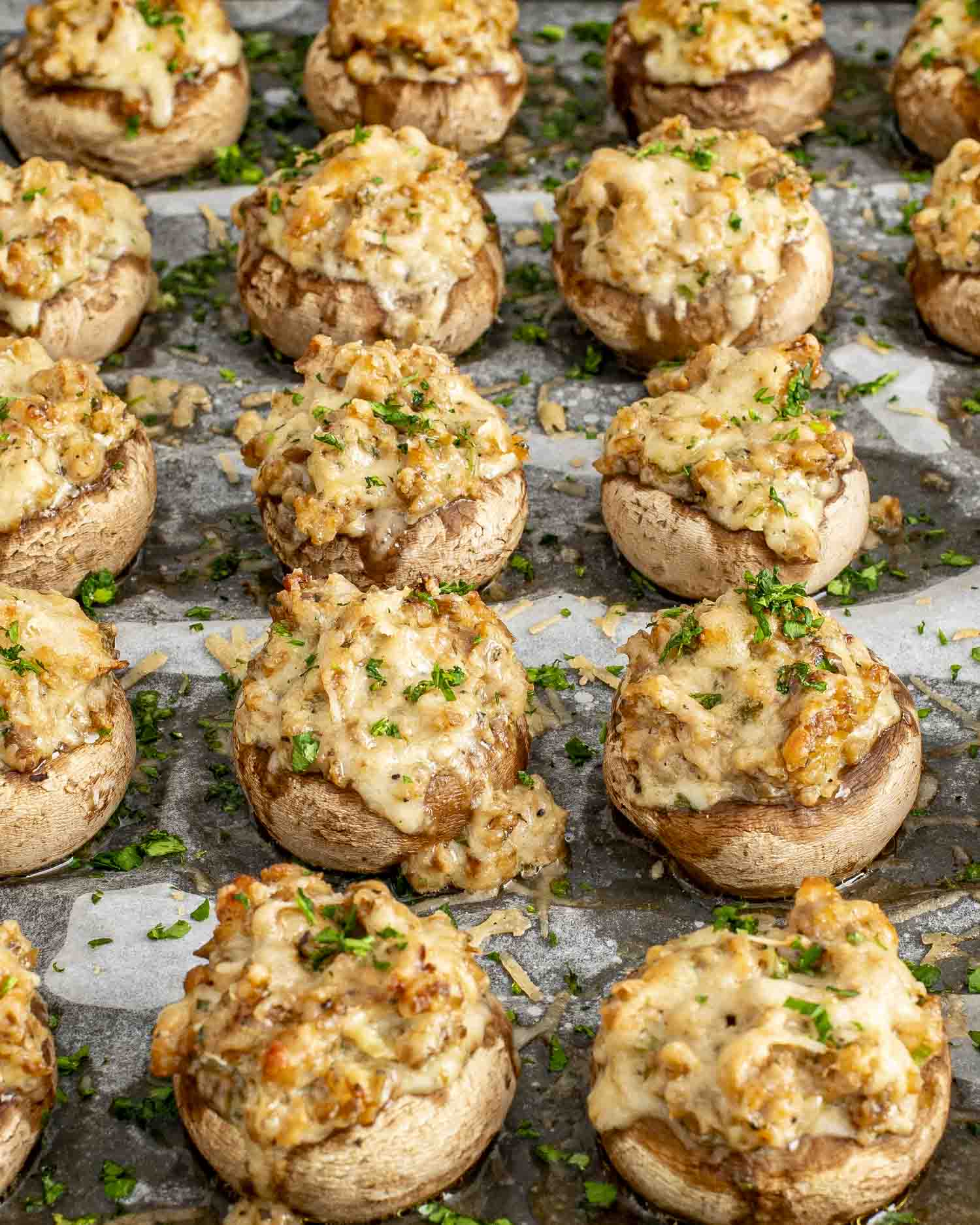 Cheesy sausage stuffed mushrooms fresh from oven on parchment, golden brown tops, sprinkled with parsley for garnish.