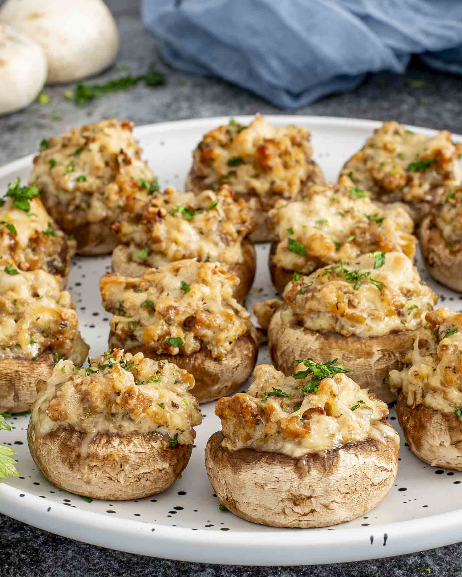 Baked cheesy sausage stuffed mushrooms on a white serving platter, topped with melted mozzarella and parsley for entertaining.