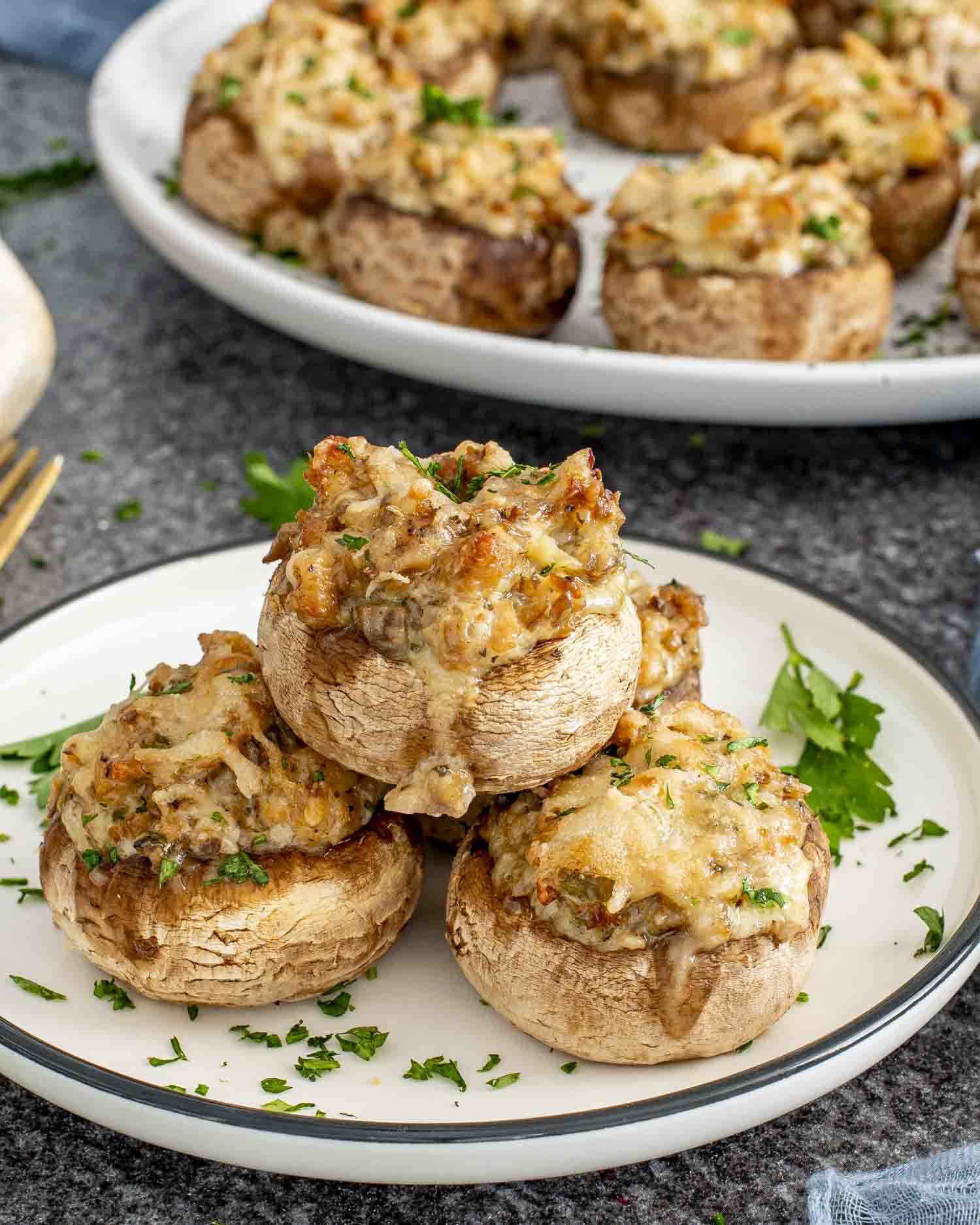 Golden brown cheesy sausage stuffed mushrooms stacked on a plate, garnished with parsley, served as an easy appetizer.