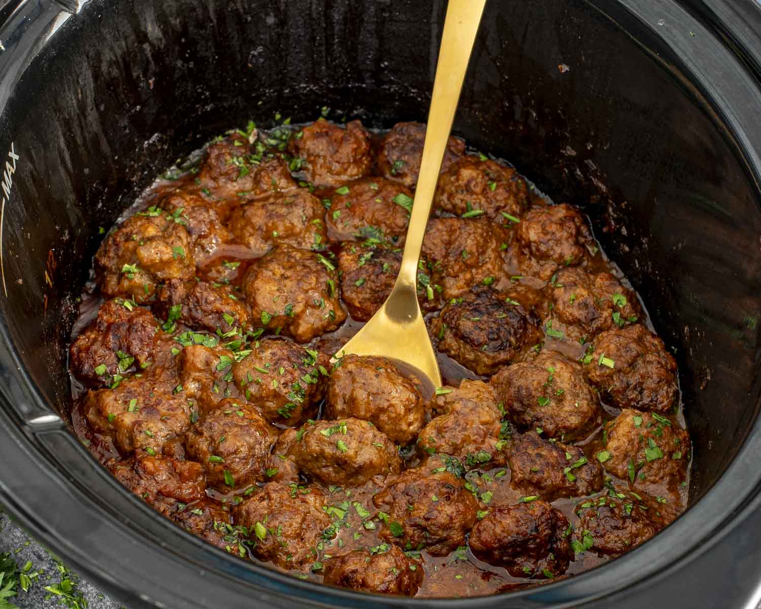 Slow cooker filled with tender Salisbury steak meatballs cooked in onion gravy, garnished with parsley, golden spoon inside.