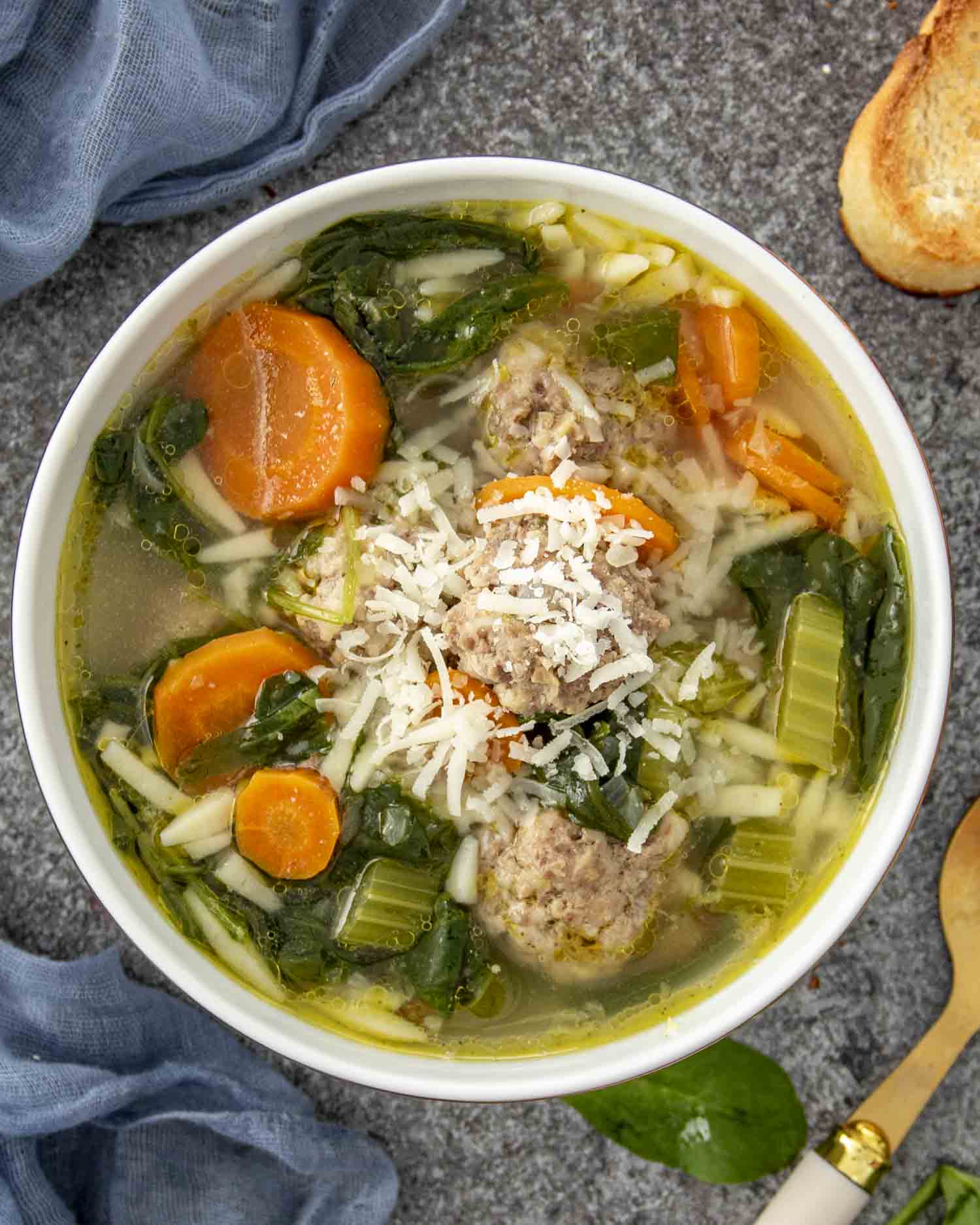 Warm bowl of Italian Wedding Soup with meatballs, orzo, carrots, spinach, and Parmesan, served on a textured stone background.
