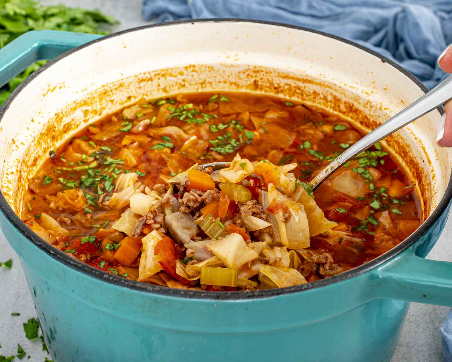 Beef and cabbage soup cooking in a Dutch oven with ground beef, cabbage, carrots, celery, and tomato-based broth.