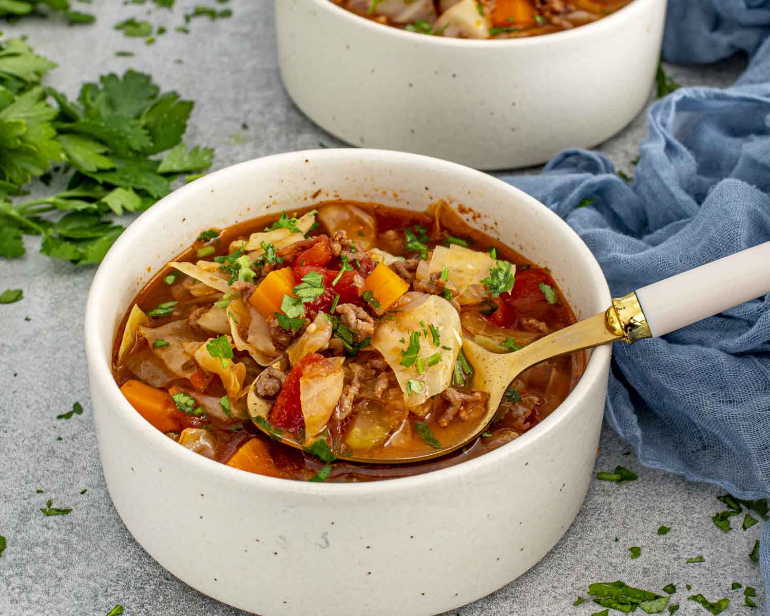 Bowl of beef and cabbage soup filled with tender cabbage, ground beef, carrots, and tomatoes, served hot with parsley.