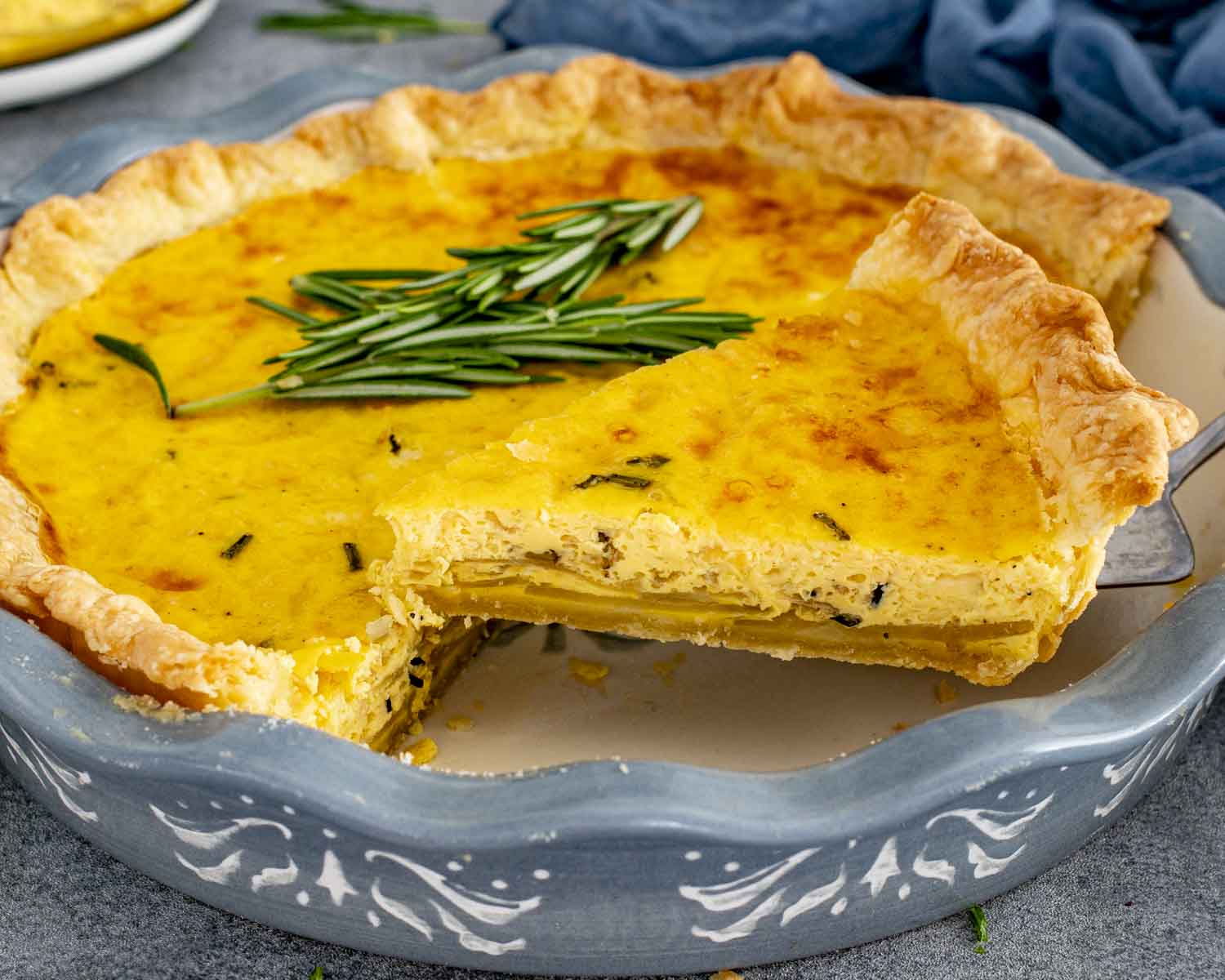 Potato rosemary cheddar quiche baked in a pie dish with golden top, flaky crust, and rosemary garnish.