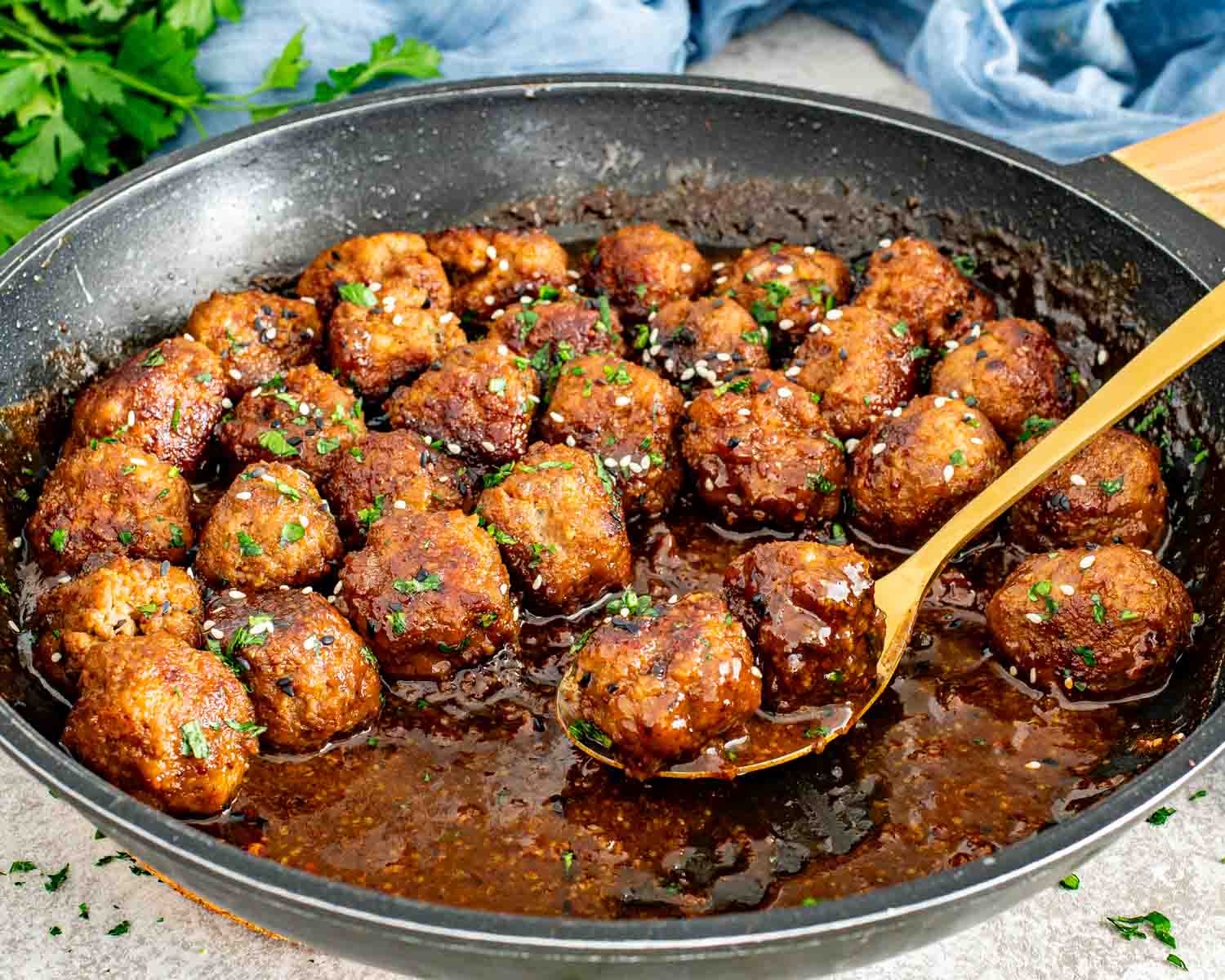 Golden maple mustard meatballs simmering in a skillet, coated evenly in thick sauce with sesame seed garnish.