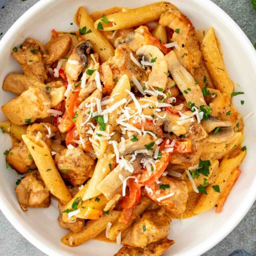 Bowl of creamy Cajun chicken pasta topped with grated Parmesan and parsley, featuring tender chicken and colorful bell peppers.