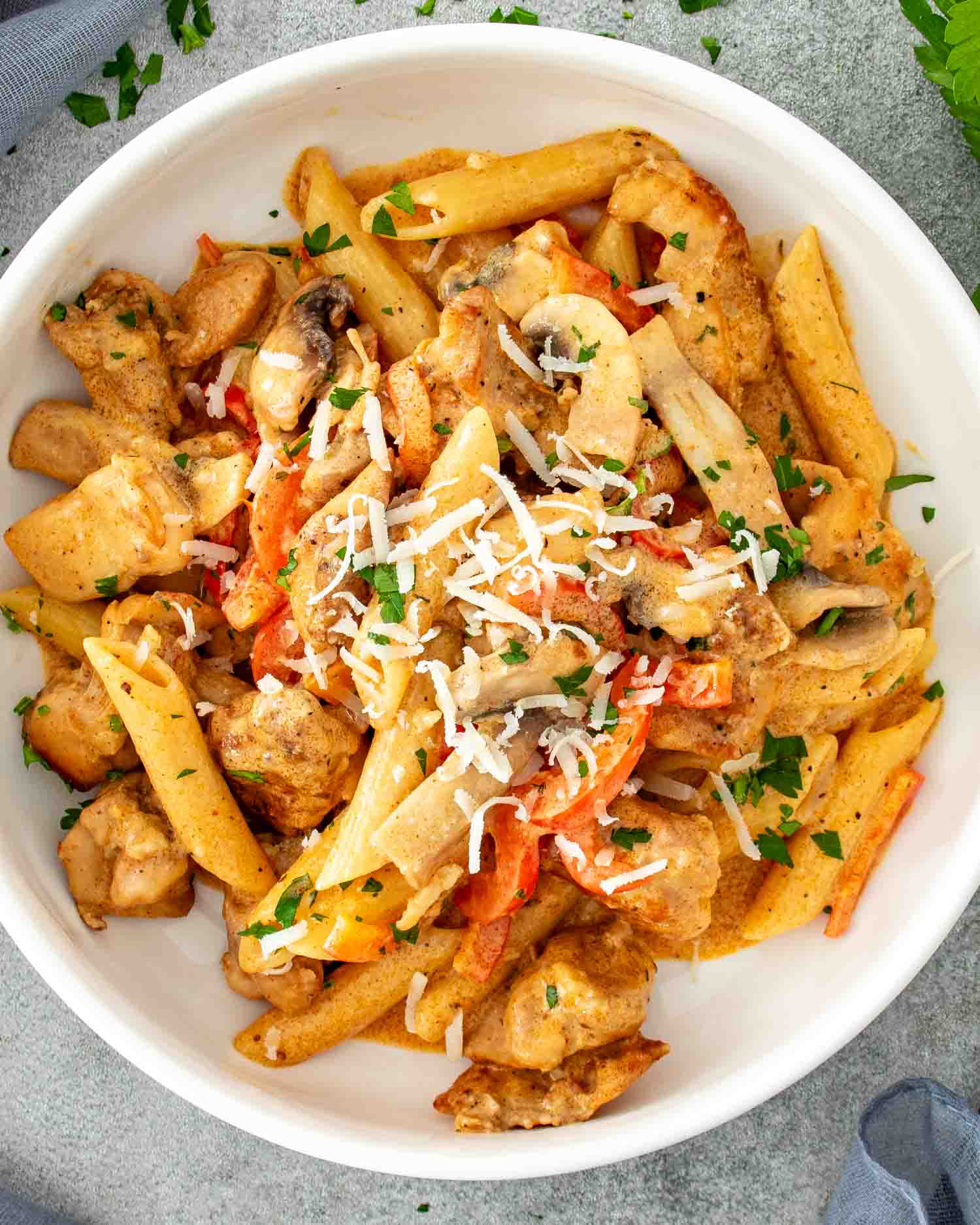 Bowl of creamy Cajun chicken pasta topped with grated Parmesan and parsley, featuring tender chicken and colorful bell peppers.