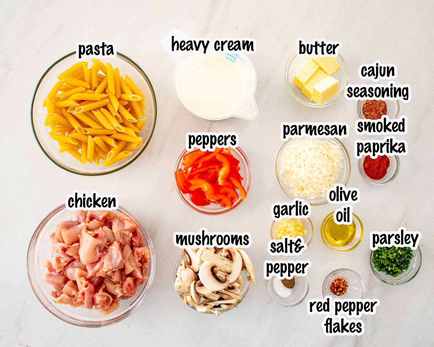 Ingredients for creamy Cajun chicken pasta including penne, chicken, heavy cream, Parmesan, bell peppers, mushrooms, garlic, and Cajun seasoning.