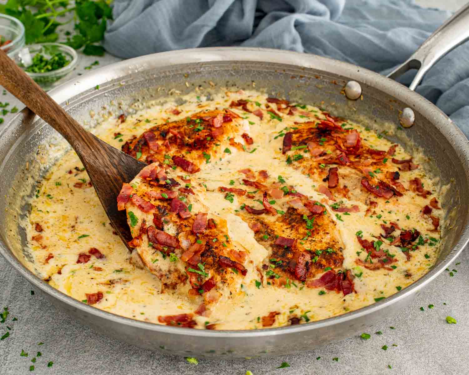 Creamy garlic parmesan chicken in a skillet being lifted with a wooden spoon, surrounded by silky parmesan cream sauce.