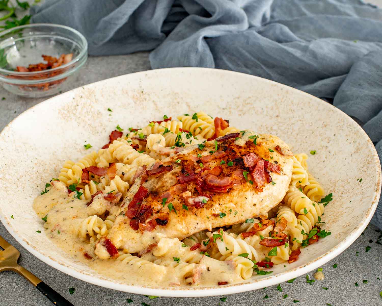 Another view of creamy garlic parmesan chicken over pasta with chopped parsley and bacon in a shallow bowl.