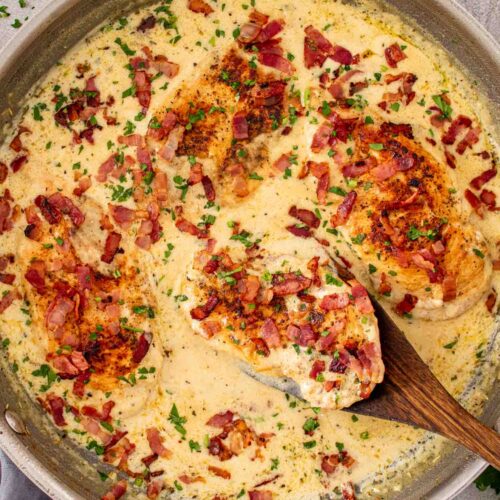 Creamy garlic parmesan chicken simmering in a skillet with golden chicken cutlets, bacon bits, parsley, and rich sauce.