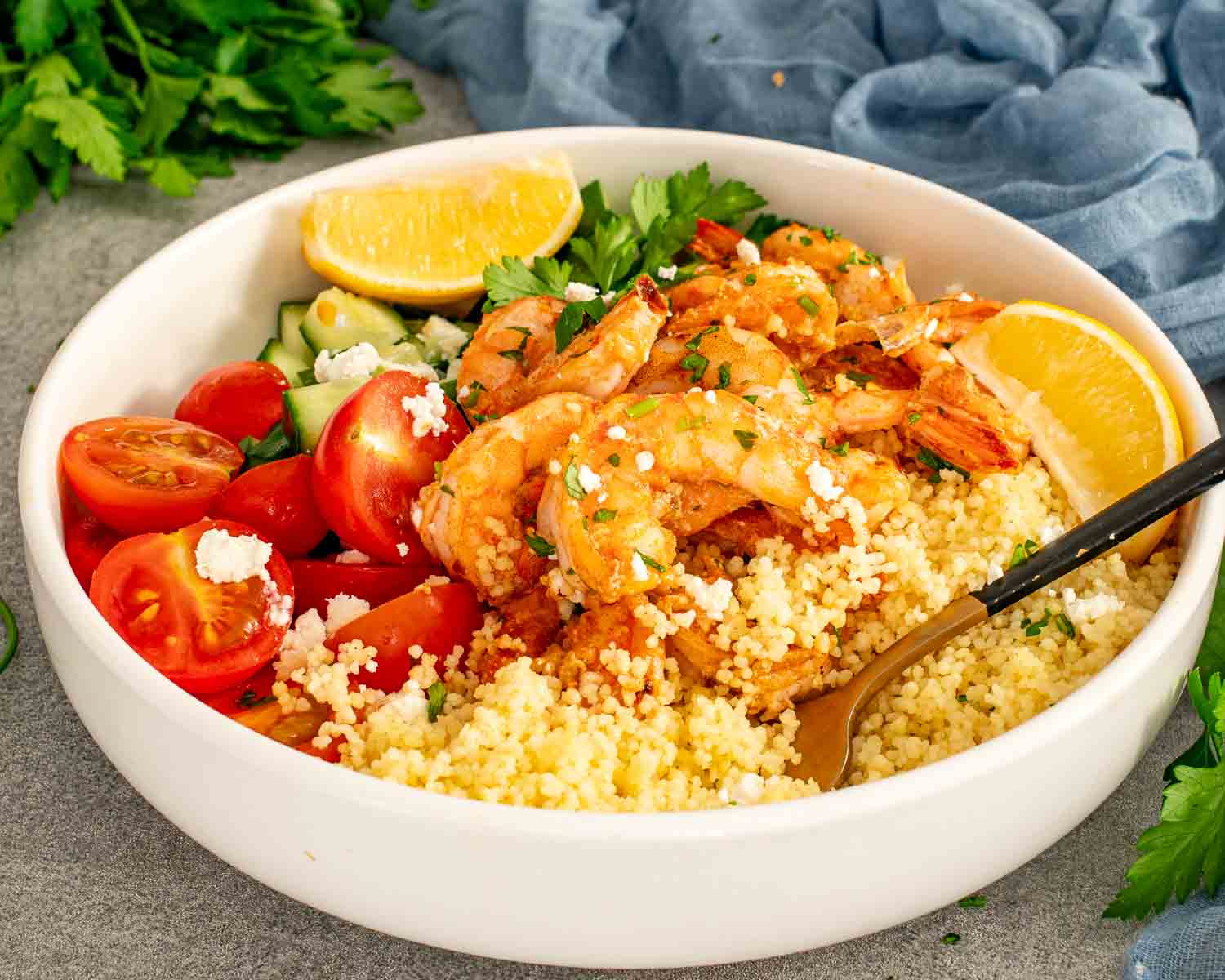 Close up garlic shrimp served over fluffy couscous with tomatoes, cucumber, feta, and fresh parsley garnish.