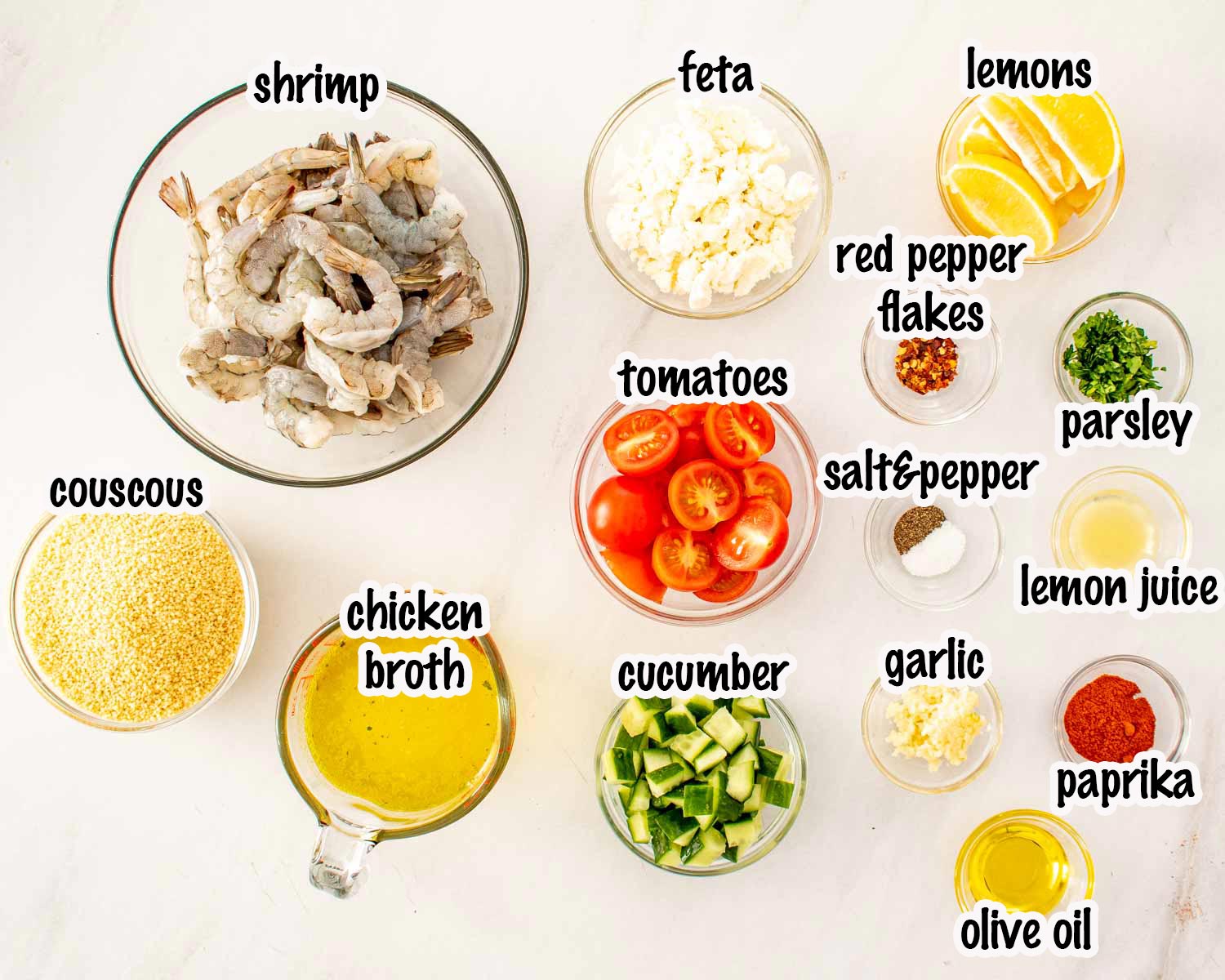 Ingredients for garlic shrimp couscous bowls including shrimp, couscous, broth, feta, tomatoes, cucumber, garlic, paprika, and lemon.
