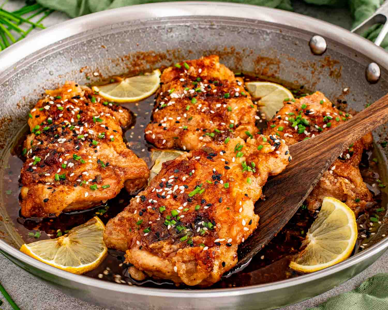 Honey lemon garlic chicken thighs in a skillet coated in glossy lemon soy sauce with sesame seeds and chives.