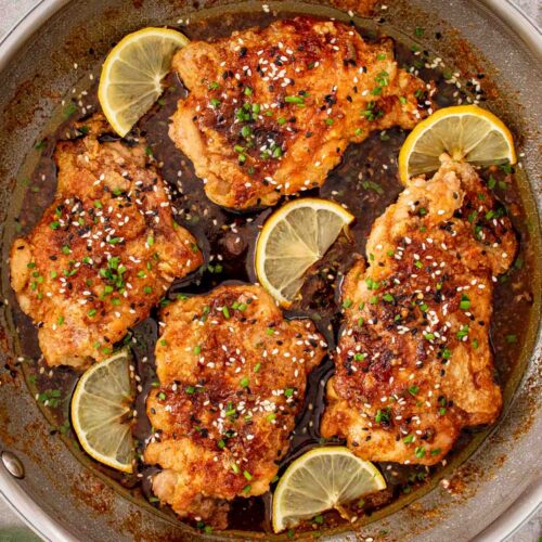 Crispy honey lemon garlic chicken thighs simmering in a garlic butter soy sauce with lemon slices.