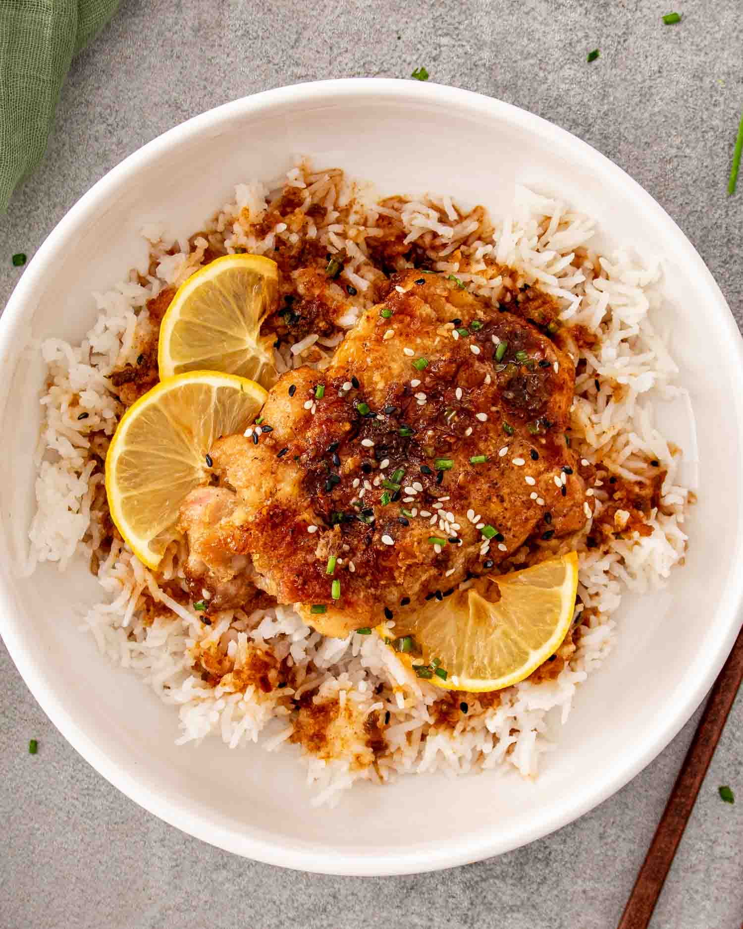 Honey lemon garlic chicken thigh served over white rice with lemon slices, sesame seeds, and chopped chives.