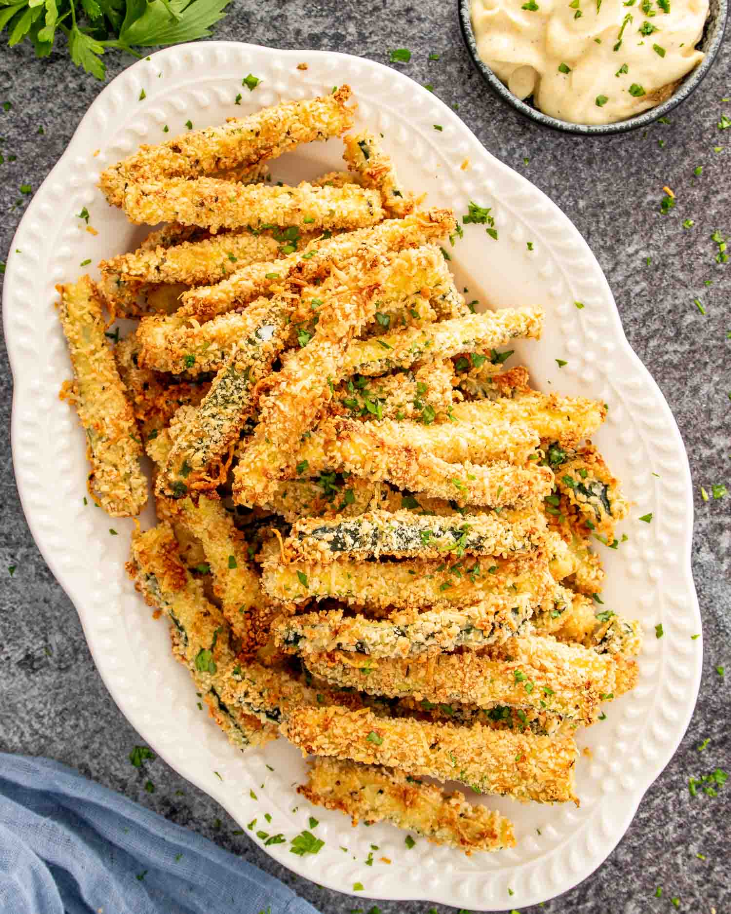 Parmesan panko crusted zucchini fries on a white serving platter with chopped parsley garnish.