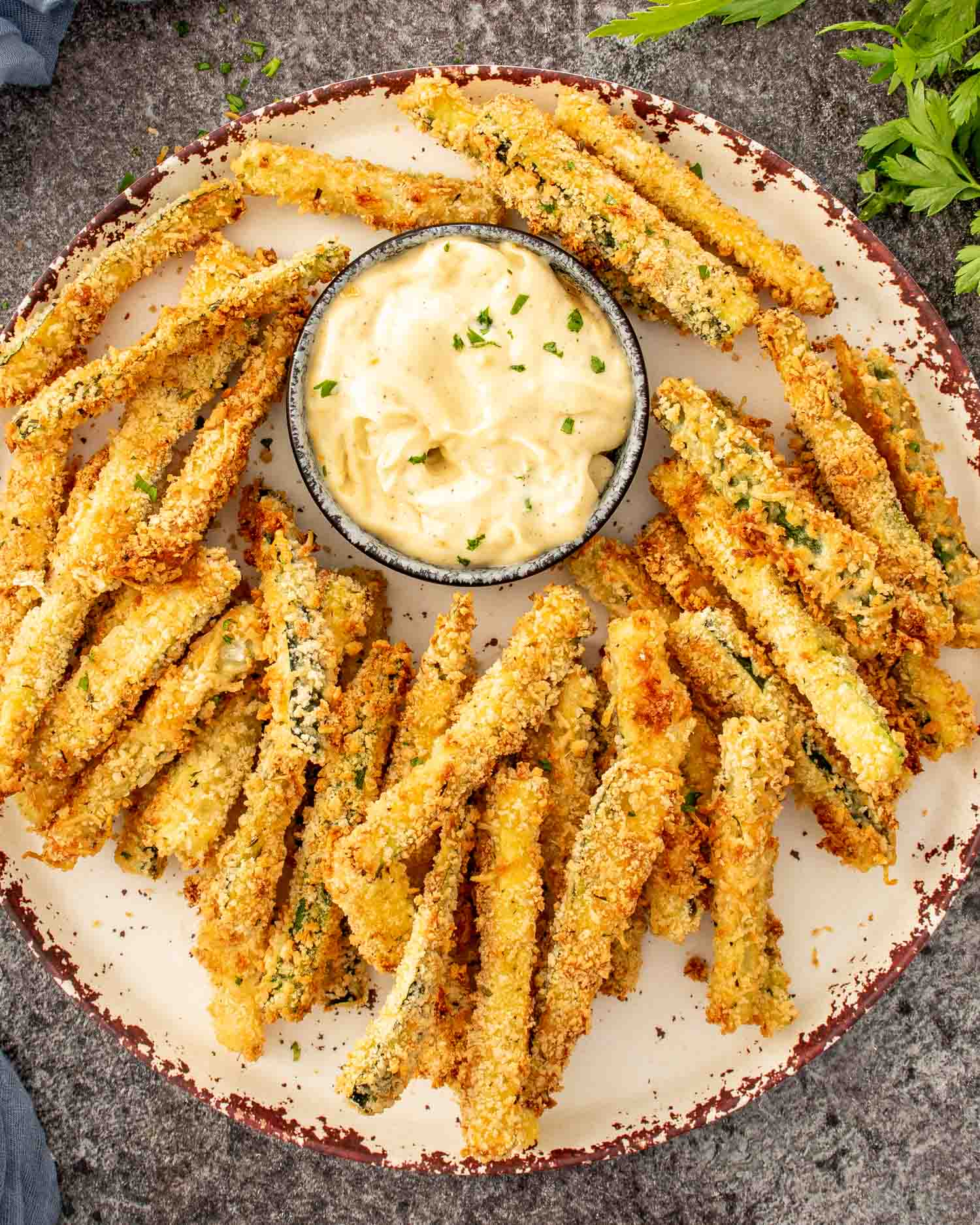 Crispy zucchini fries arranged on a rustic platter with creamy garlic aioli dip in the center.