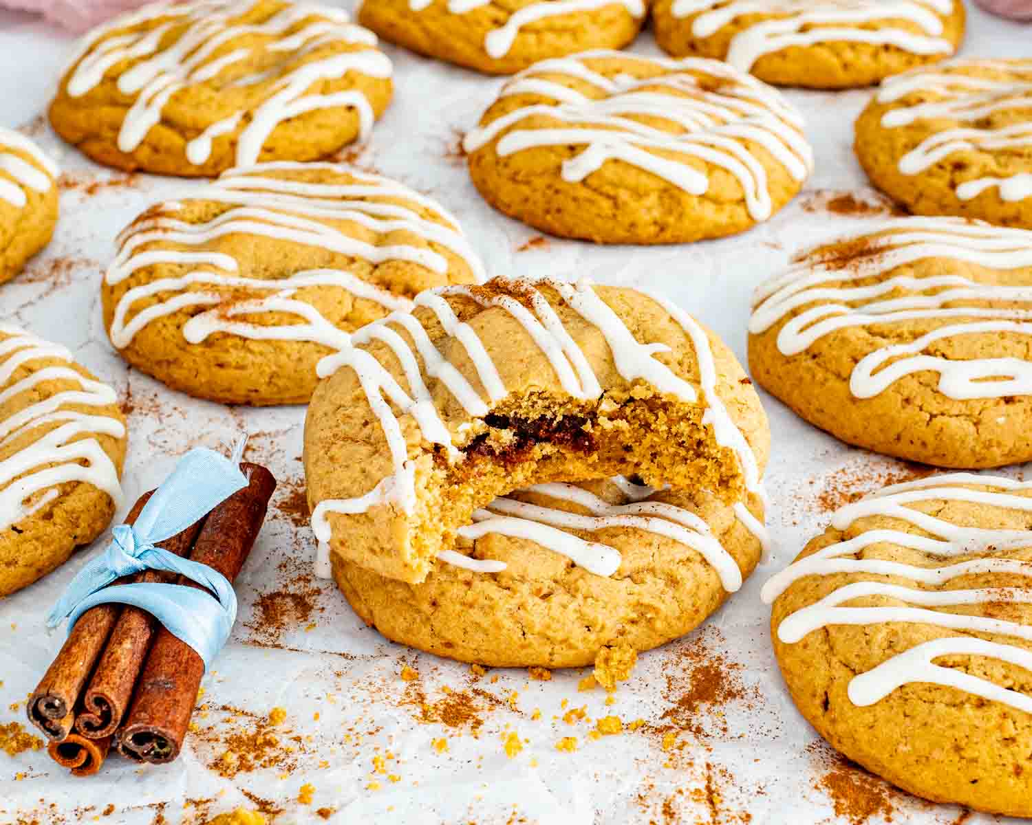Cinnamon roll cookies on parchment paper with cream cheese glaze, one broken open showing soft cinnamon sugar filling inside.