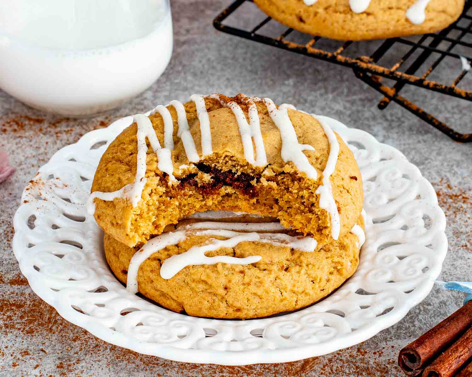 Close up of cinnamon roll cookies stacked on plate with thick glaze and visible cinnamon filling inside soft golden cookie.