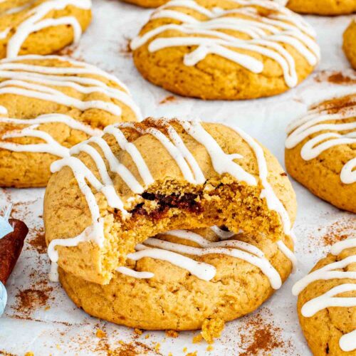 Close up cinnamon roll cookie broken open showing soft cinnamon filling and thick cream cheese glaze drizzled over top.