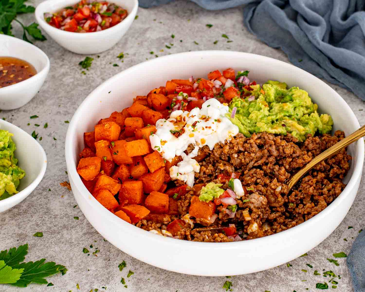 Hot honey taco beef bowl with roasted sweet potatoes, seasoned ground beef, mashed avocado, tomato salsa, and cottage cheese.