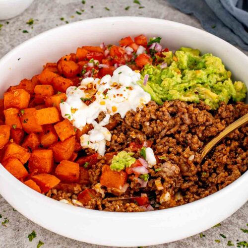 Hot honey taco beef bowl with roasted sweet potatoes, seasoned ground beef, mashed avocado, tomato salsa, and cottage cheese.