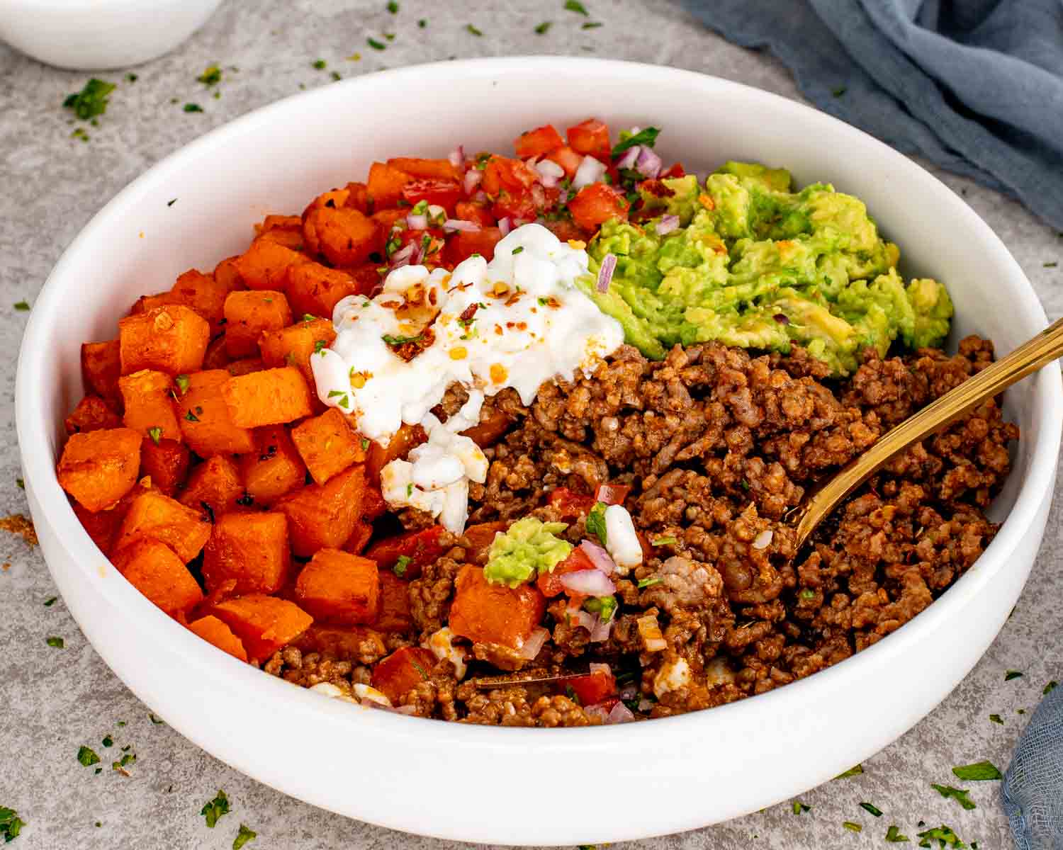 Hot honey taco beef bowl with roasted sweet potatoes, seasoned ground beef, mashed avocado, tomato salsa, and cottage cheese.