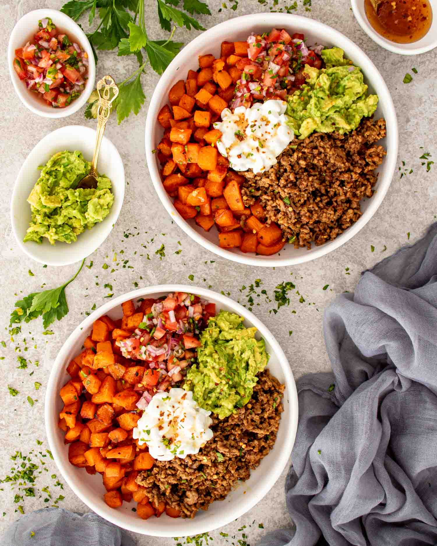 Two hot honey taco beef bowls with roasted sweet potatoes, taco beef, avocado, fresh tomato salsa, and cottage cheese.