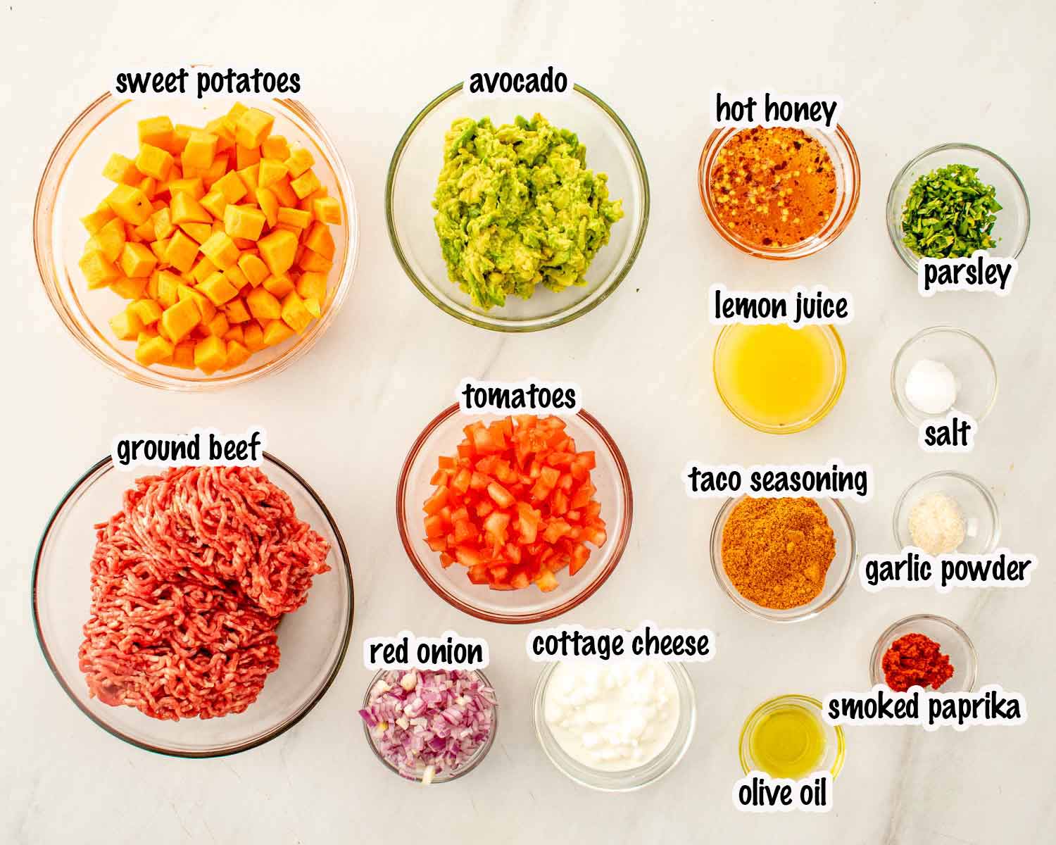 Overhead ingredient shot for hot honey taco beef bowls with ground beef, sweet potatoes, avocado, tomatoes, cottage cheese, taco seasoning.