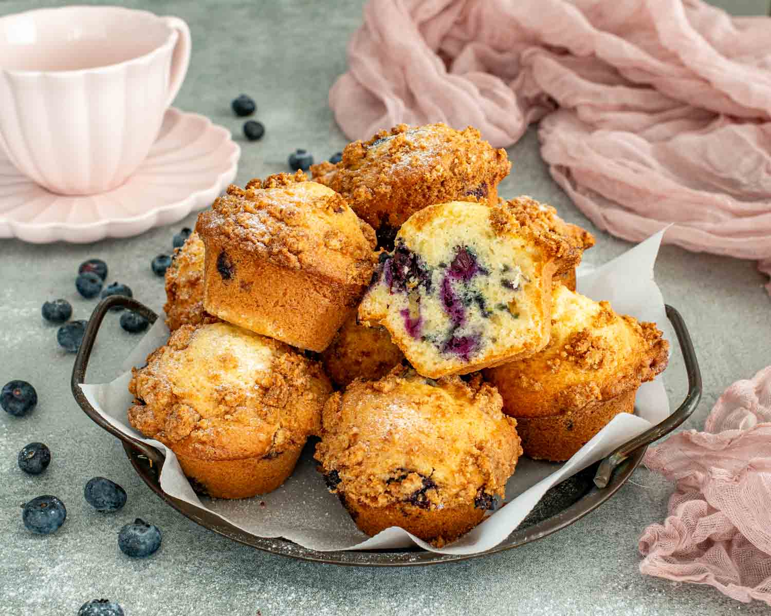 Close up of blueberry crumb muffin half on white plate showing soft crumb texture and baked blueberries inside muffin.