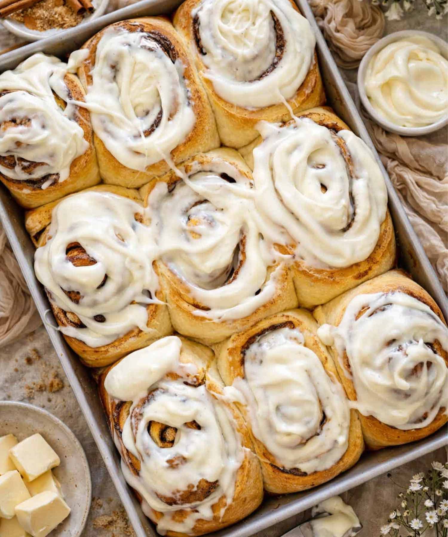 A top down view of nine jumbo bakery style cinnamon rolls in a pan covered in thick cream cheese frosting.