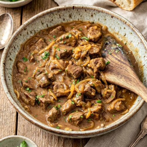 Bowl of beef and onion skillet with tender beef, caramelized onions, and thick gravy served with crusty bread on the side.